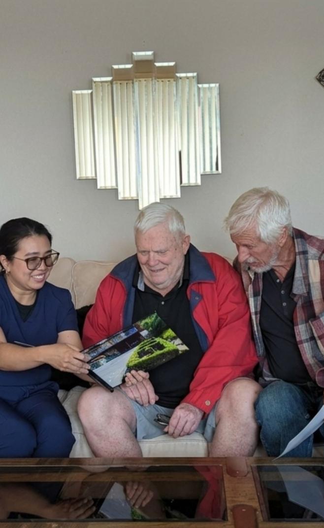 Caregiver reviewing care information with two senior men on a sofa